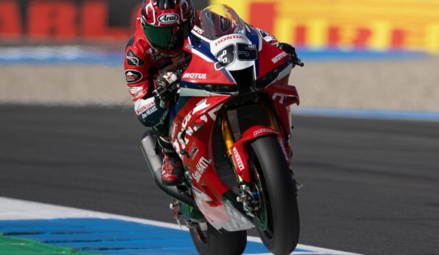 Racing rider in red gear on a red Honda motorcycle leaning into a turn on a race track.