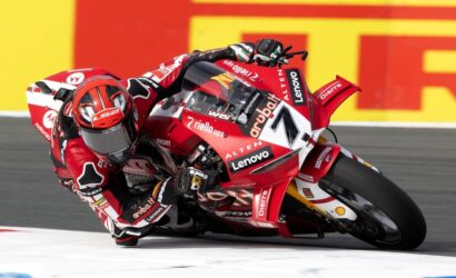 MotoGP rider in red suit leaning into a left-hand corner on a red Ducati bike during a race.