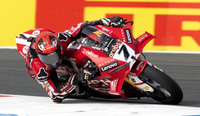 MotoGP rider in red suit leaning into a left-hand corner on a red Ducati bike during a race.