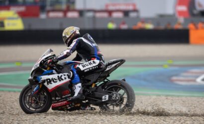 Racer in full gear on a Rokit-branded motorcycle leaning into a turn on a gravel run-off at a race track