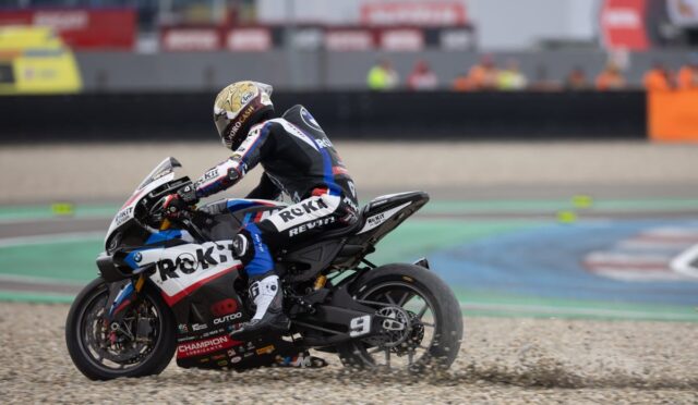 Racer in full gear on a Rokit-branded motorcycle leaning into a turn on a gravel run-off at a race track