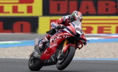 MotoGP rider in a red racing suit leaning into a corner on a red Honda motorcycle with number 93 shown on the front.