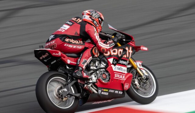 MotoGP rider on a red Ducati racing bike leaning into a turn on a race track, sponsor logos visible across suit and bike