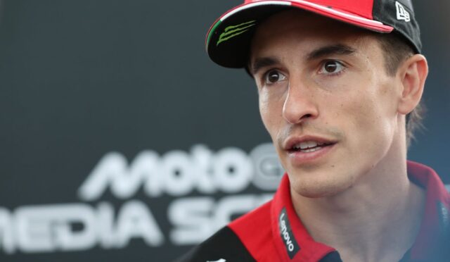 Close-up of a young racing driver in a red cap and team polo, speaking during a media interview at a race event.