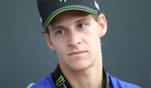 Young man wearing a black Monster energy cap and blue jacket, looking to the left.