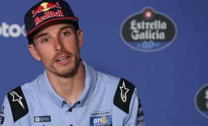 Racer wearing a Red Bull cap speaks at a press conference against a blue backdrop.