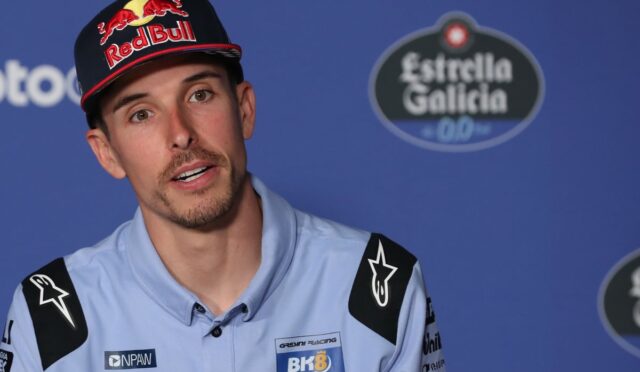 Racer wearing a Red Bull cap speaks at a press conference against a blue backdrop.