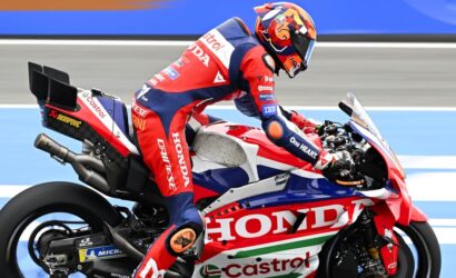 Rider in red, white, and blue Honda racing gear on a red Honda race bike, leaning into a turn on a racetrack.