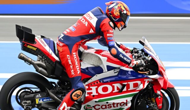 Rider in red, white, and blue Honda racing gear on a red Honda race bike, leaning into a turn on a racetrack.