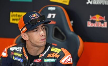 Motocross rider in KTM gear sits in a race chair in the pit area, nose bandage on his nose.
