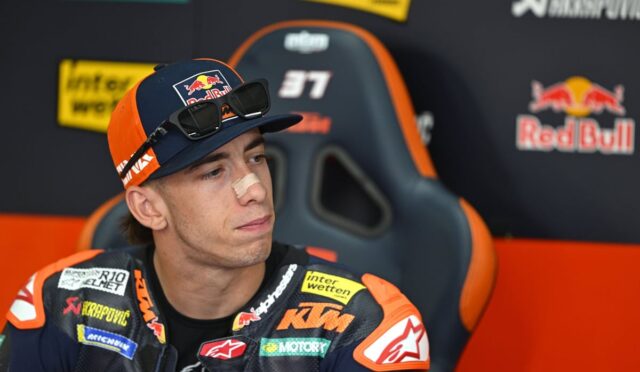 Motocross rider in KTM gear sits in a race chair in the pit area, nose bandage on his nose.