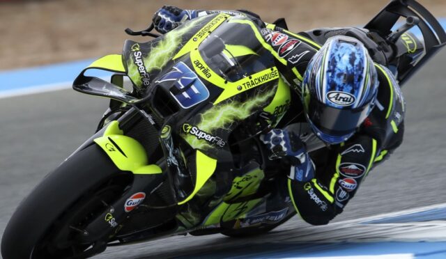 Motorcycle racer in a neon-yellow racing suit and bike leaning into a turn on a track, helmeted with blue visor and sponsor logos visible.