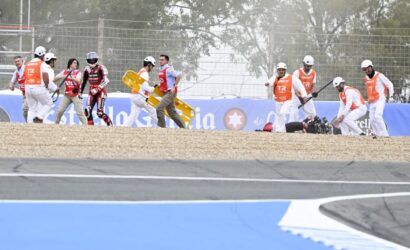 Trackside safety crew carrying a yellow spine board toward a race car incident.