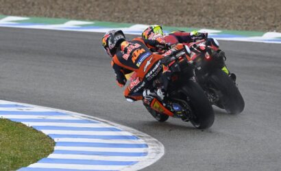 Two MotoGP riders lean into a wet corner, the leading bike a Red Bull KTM in orange and blue livery.