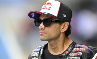 Moto racer in a Red Bull cap and dark sunglasses, wearing a branded leather racing suit with sponsor logos.