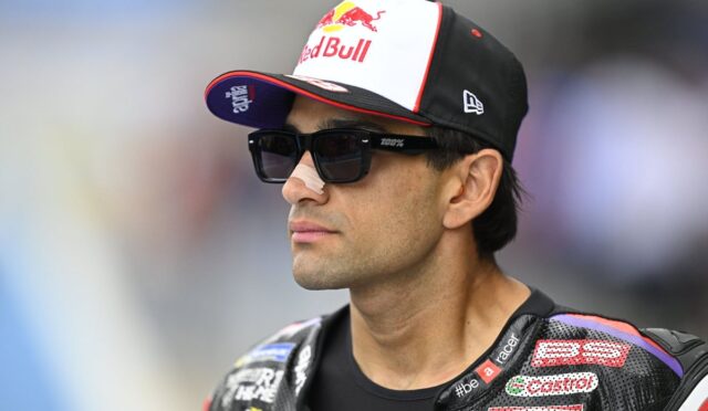 Moto racer in a Red Bull cap and dark sunglasses, wearing a branded leather racing suit with sponsor logos.