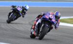 Two sport motorcycles lean into a left-hand turn on a race track; the lead bike is purple with red and white decals.
