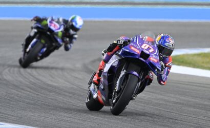 Two sport motorcycles lean into a left-hand turn on a race track; the lead bike is purple with red and white decals.