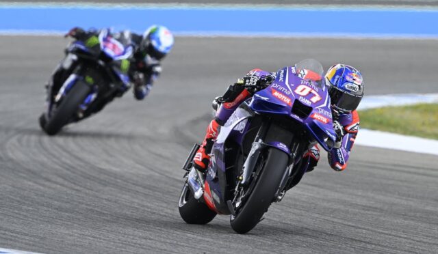 Two sport motorcycles lean into a left-hand turn on a race track; the lead bike is purple with red and white decals.