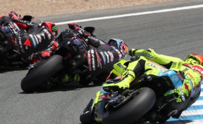 Motorcycle racers leaning into a sharp turn on a race track, colorful leathers and bikes in close formation.