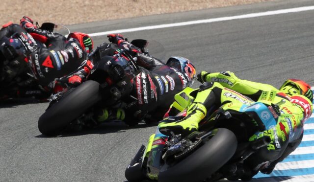 Motorcycle racers leaning into a sharp turn on a race track, colorful leathers and bikes in close formation.