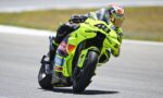 MotoGP rider in a neon yellow-green suit leans into a left turn on a bright yellow-green race bike on a track.