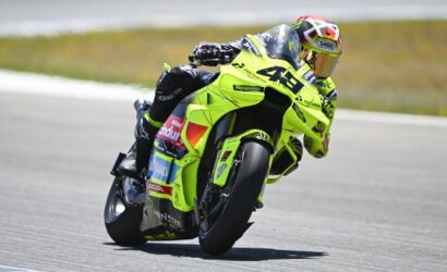 MotoGP rider in a neon yellow-green suit leans into a left turn on a bright yellow-green race bike on a track.