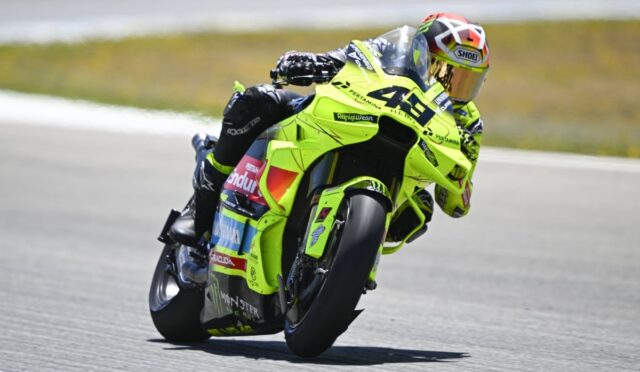 MotoGP rider in a neon yellow-green suit leans into a left turn on a bright yellow-green race bike on a track.