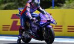 Rider in purple racing suit on a purple motorcycle leaning into a turn on a track, number 43 visible on the bike with yellow barriers in the background.