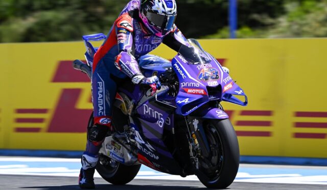 Rider in purple racing suit on a purple motorcycle leaning into a turn on a track, number 43 visible on the bike with yellow barriers in the background.