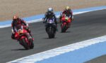 Three motorcycle racers lean into a curve on a racetrack, rider #10 in front, followed by #46 and a blue Yamaha rider behind.*