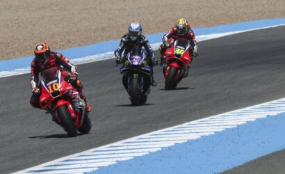 Three motorcycle racers lean into a curve on a racetrack, rider #10 in front, followed by #46 and a blue Yamaha rider behind.*