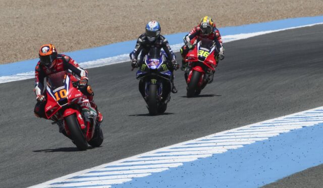 Three motorcycle racers lean into a curve on a racetrack, rider #10 in front, followed by #46 and a blue Yamaha rider behind.*