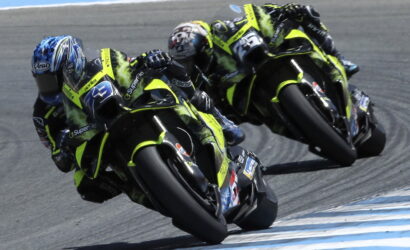 Three neon-yellow racing motorcycles lean into a sharp left turn on a race track, riders in matching leathers closely grouped.