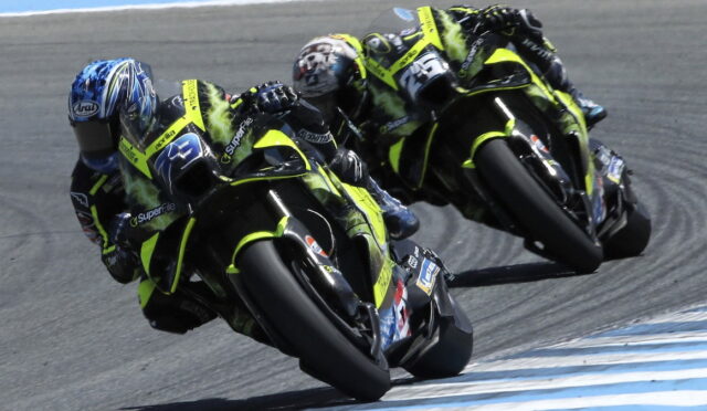 Three neon-yellow racing motorcycles lean into a sharp left turn on a race track, riders in matching leathers closely grouped.