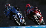 Two motorcycle racers in blue and red leathers leaning into a curve on a racetrack.