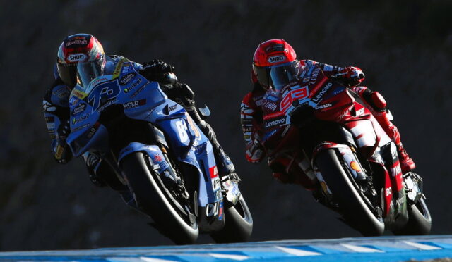 Two motorcycle racers in blue and red leathers leaning into a curve on a racetrack.