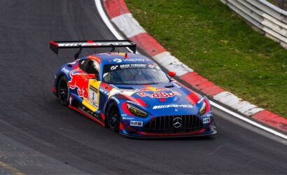 Race car with Red Bull livery (Mercedes-AMG) cornering on a track, large rear wing visible in a red/white curbstone section of the circuit.