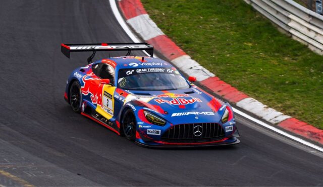 Race car with Red Bull livery (Mercedes-AMG) cornering on a track, large rear wing visible in a red/white curbstone section of the circuit.