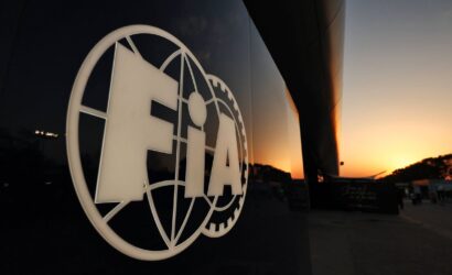 Close-up of a white globe-and-gear logo on a dark reflective wall, with a sunset sky in the background.|