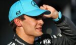 Close-up of a driver in a turquoise cap with a Mercedes logo, speaking into a FIA microphone, number 63 on the side of the cap.