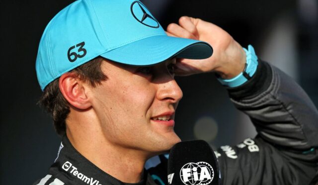 Close-up of a driver in a turquoise cap with a Mercedes logo, speaking into a FIA microphone, number 63 on the side of the cap.