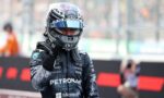 Formula 1 driver in Petronas racing suit and helmet raises a fist on the track with blurred grandstands behind him.