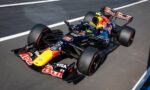 Red Bull Racing Formula 1 car on a race track with sponsor logos visible on the body and front wing, viewed from above.