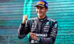 Mercedes race driver in a Petronas suit on a podium, smiling and raising a clenched fist in celebration.
