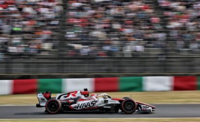 Formula 1 race car speeding on a track with a blurred grandstand and Italian flag-pattern barriers in the background.