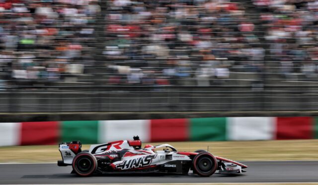 Formula 1 race car speeding on a track with a blurred grandstand and Italian flag-pattern barriers in the background.