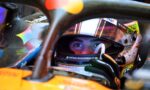 Close-up of a race car driver wearing a colorful helmet, peering through the cockpit opening.