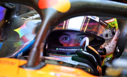 Close-up of a race car driver wearing a colorful helmet, peering through the cockpit opening.