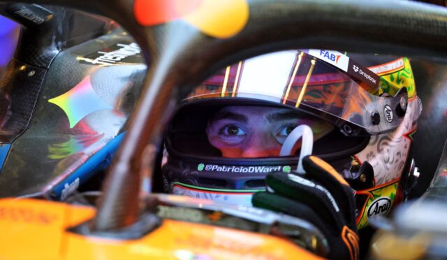 Close-up of a race car driver wearing a colorful helmet, peering through the cockpit opening.